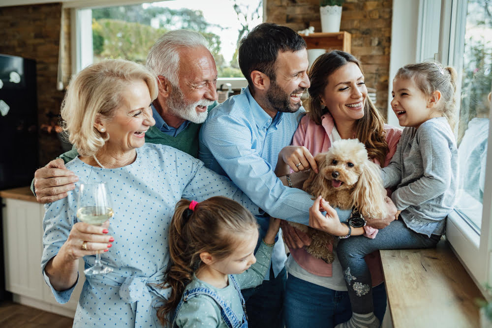 Família feliz com pessoas de diferentes idades, sorrindo em frente a uma janela